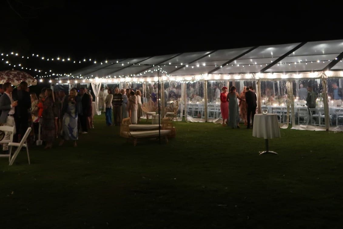 Clear-roof marquee with festoon lighting and dry bars on a lawn at night